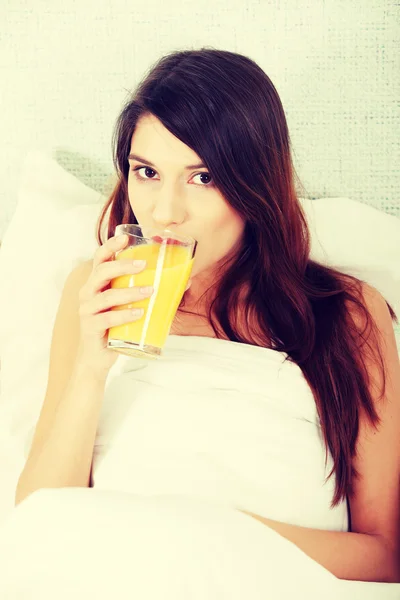 Mulher na cama bebendo suco de laranja — Fotografia de Stock