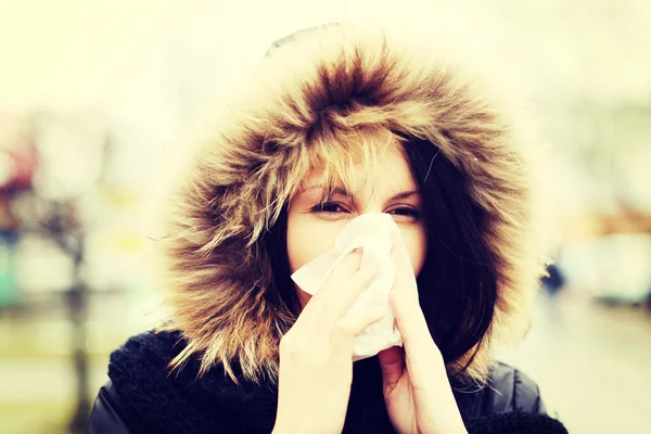 Young woman sneezes during cold day.