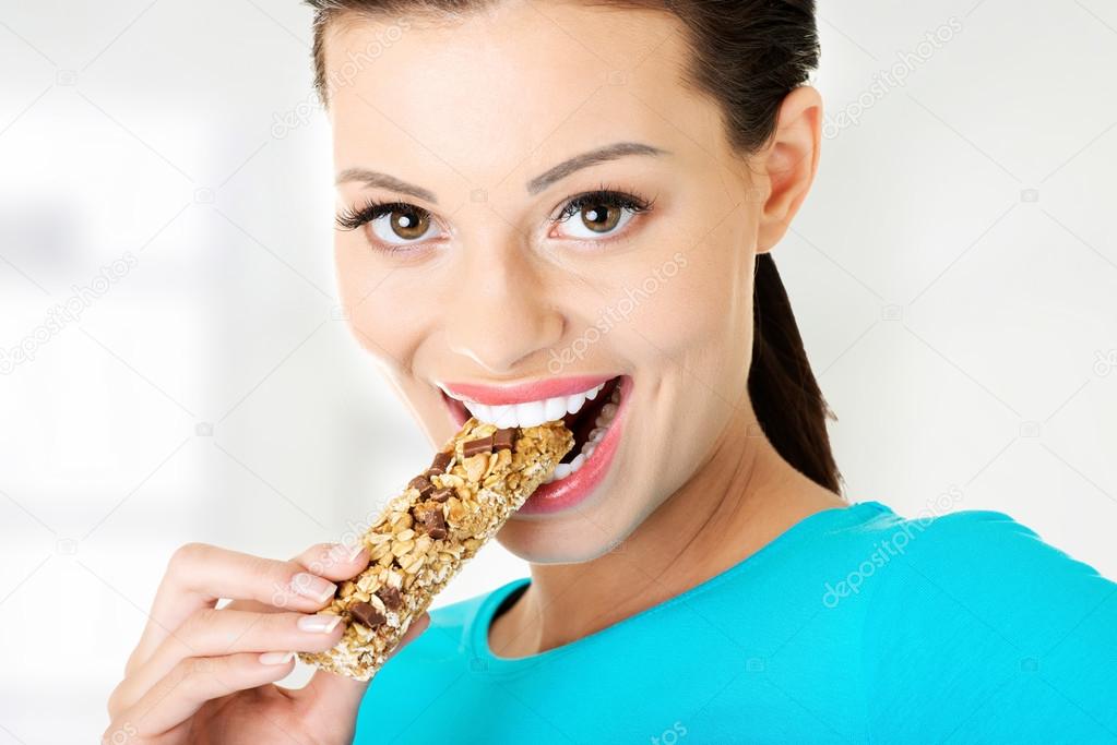 Young woman eating cereal candy bar