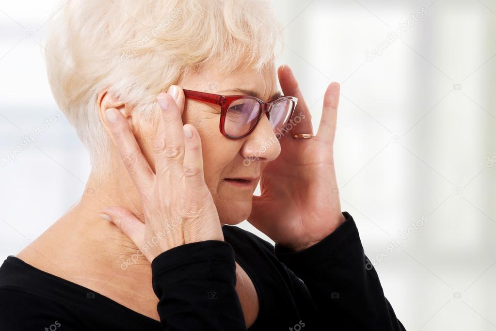 An old woman is eye glasses is having a headache.
