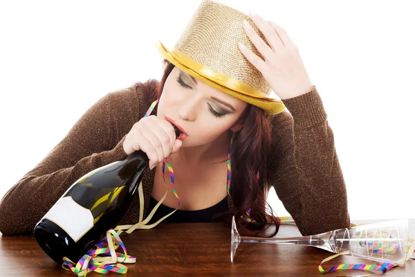 Jonge dronken vrouw door een tabel en met lege fles. — Stockfoto