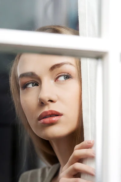 Mujer hermosa está mirando a través de la ventana . — Foto de Stock