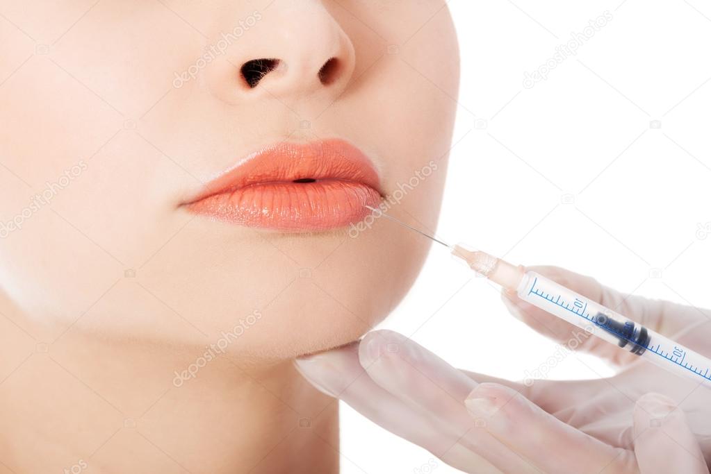 Young beautiful woman doing injection into mouth.