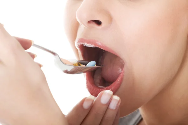 Beautiful young woman eating pills ona spoon. — Stock Photo, Image