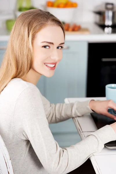 Mujer sentada junto a la mesa con portátil y taza . — Foto de Stock