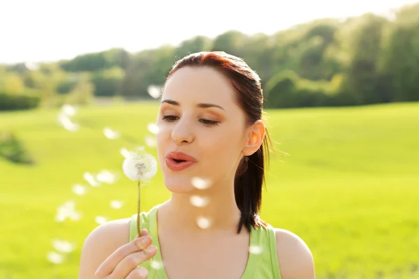 Woman blowing on a dandelion — Stock Photo, Image