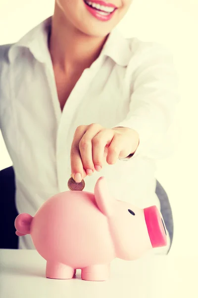 Empresária colocando uma moeda em um banco porquinho — Fotografia de Stock