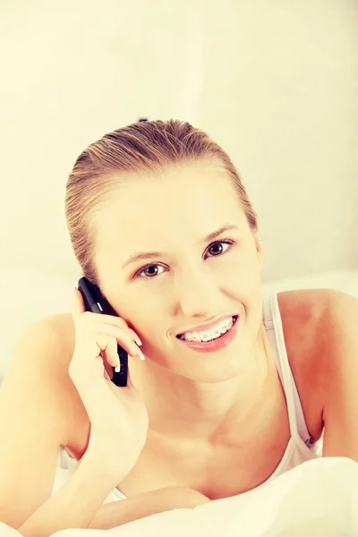 Bella donna con il telefono cellulare sdraiato sul letto — Foto Stock