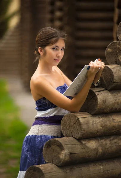 Girl with the book at the wall of wooden house — Stock Photo, Image