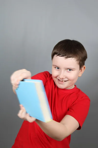 Cheerful boy fights book, gray background — Stock Photo, Image