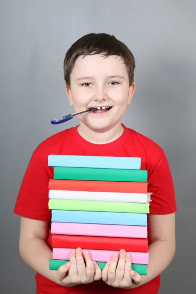 Niño con un bolígrafo en la boca sosteniendo una pila de libros — Foto de Stock