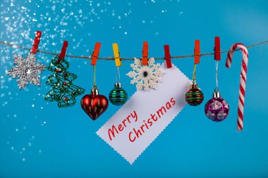 Noel süsleri mavi arka planda bir ipte asılı duruyor. Mesajın için yer aç. Noel kartı..