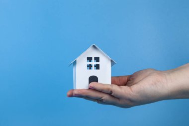 Rent apartments, Real Estate and buying a house idea. Blue background.Hand with a toy house.