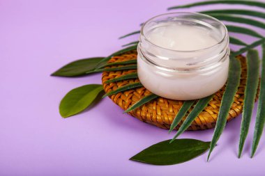 SPA natural organic cosmetics for personal hygiene. Skin cream and oil in cosmetic bottles, green leaf on rattan container in bathroom.Lilac background.