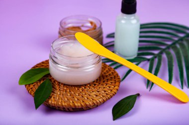 SPA natural organic cosmetics for personal hygiene. Skin cream and oil in cosmetic bottles, green leaf on rattan container in bathroom.Lilac background.
