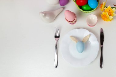 Paskalya sofrası ve sarı çiçekli akşam yemeği, şenlikli süslemeler, beyaz kuş ve çok renkli yumurtalar. Tavşan kulaklı bir Paskalya yumurtası. Kapat..
