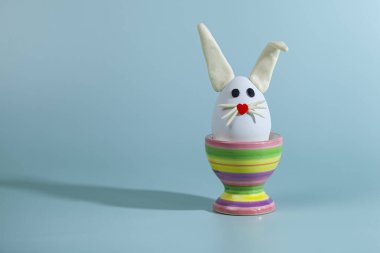  Paskalya tebrik kartı. Kürsüde tavşan kulaklı Paskalya yumurtası. Yeşil arkaplan, metin için yer.