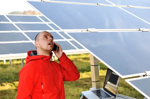 Engineer working with laptop by solar panels, talking on cell phone — Stock Photo, Image