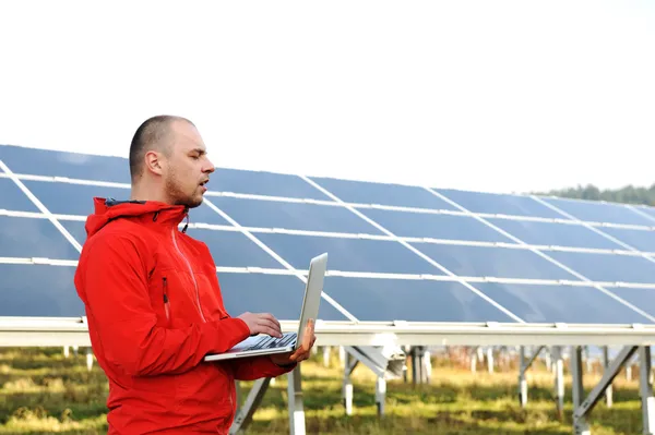 Male engineer using laptop, solar panels in background Stock Image