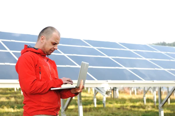 Male engineer using laptop, solar panels in background Royalty Free Stock Photos