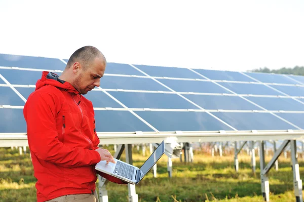 Male engineer using laptop, solar panels in background Royalty Free Stock Images