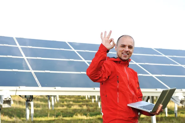 Male engineer using laptop, solar panels in background Stock Photo