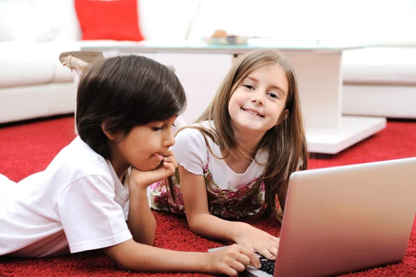 Klein meisje en jongen liggen met laptop thuis op de grond Stockfoto