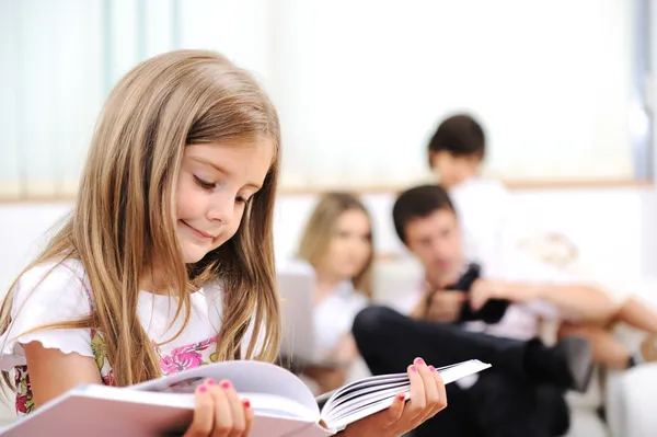 Niña leyendo en casa, interior con familia feliz — Foto de Stock