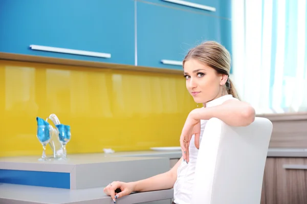Unga vackra blonda kvinnan i köket sitter på stol — Stockfoto