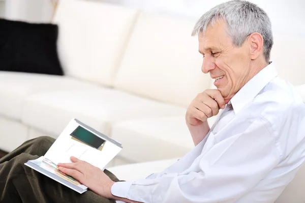 Oudere man ontspannen, lezen tijdschrift in woonkamer — Stockfoto