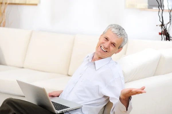 Ontspannen senior man met laptop op de Bank glimlachen — Stockfoto