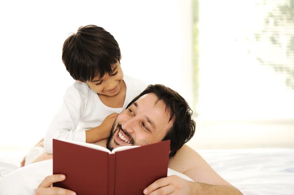 Pai e filho na cama, lendo livro juntos — Fotografia de Stock