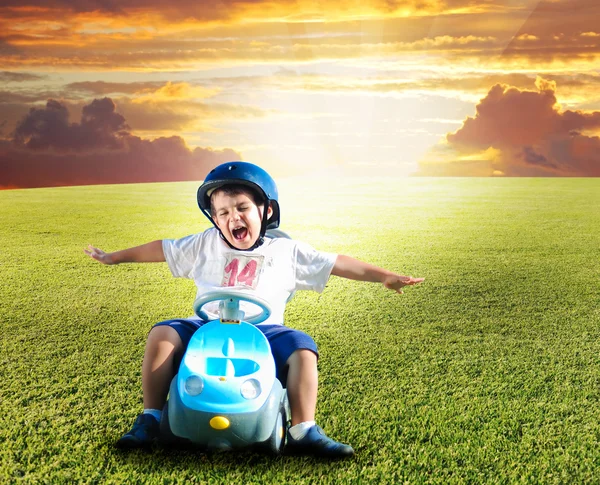 Happy kid on green meadow driving a car — Stock Photo, Image