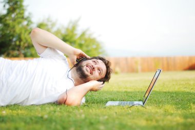 dizüstü bilgisayar ile yeşil çayır üzerinde mutlu bir genç adam