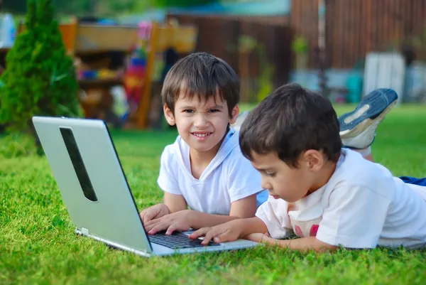 Twee schattige kinderen leggen in gras op laptop — Stockfoto