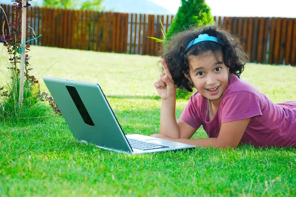 En liten söt flicka fastställande i gräset med laptop — Stockfoto