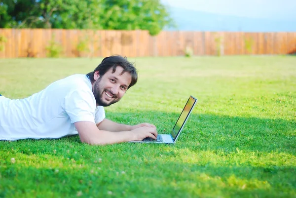 Happy young man working on laptop in beautiful green enviroment — Stock Photo, Image