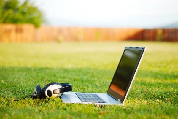 Laptop e fone de ouvido em terreno verde — Fotografia de Stock
