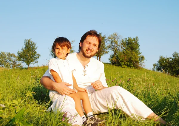 Młody ojciec w kolorze białym z dzieckiem na pięknej łące — Zdjęcie stockowe