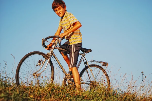 El chico está a punto de sentarse en su bicicleta al aire libre. Imagen De Stock