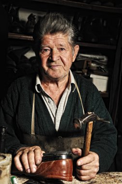 Old man, shoemaker, repairing old handmade shoe in his workshop clipart