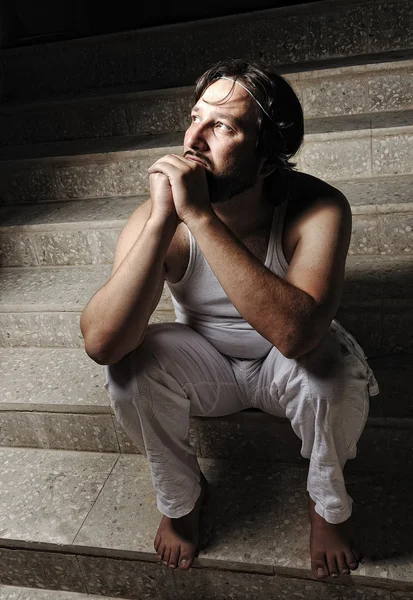 Thoughtful man on black background in low key, sitting on stairs — Stock Photo, Image