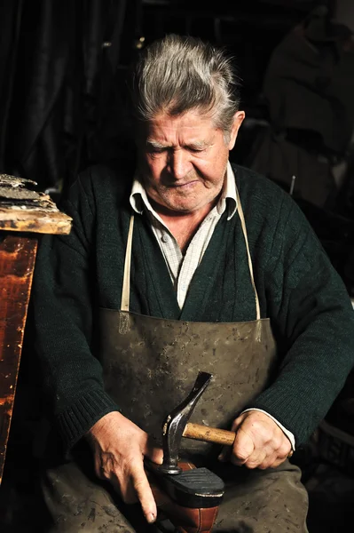 Пожилой человек, сапожник чинит старые ботинки в мастерской — стоковое фото