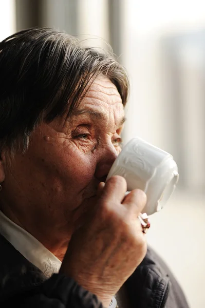 Портрет пожилой женщины, смотрящей в окно и пьющей кофе — стоковое фото