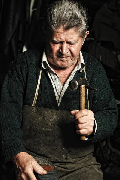 Old man, shoemaker, repairing old handmade shoe in his workshop Stock Photo