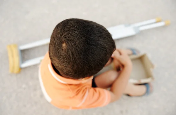 Hongerig kind bedelen op straat met een krukken naast — Stockfoto