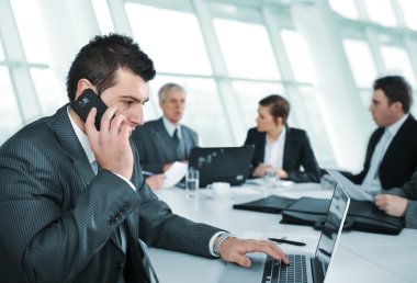 Business man speaking on the phone while in a meeting clipart