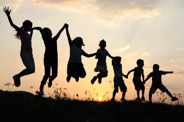 Silhueta, grupo de crianças felizes brincando no prado, pôr do sol, verão — Fotografia de Stock