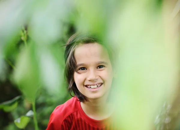 Retrato de perto de um menino feliz escondido em braços de árvore e l — Fotografia de Stock