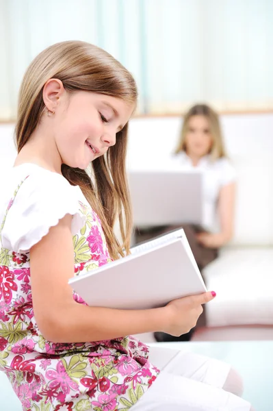 Little girl reading in home with mother — Stock Photo, Image